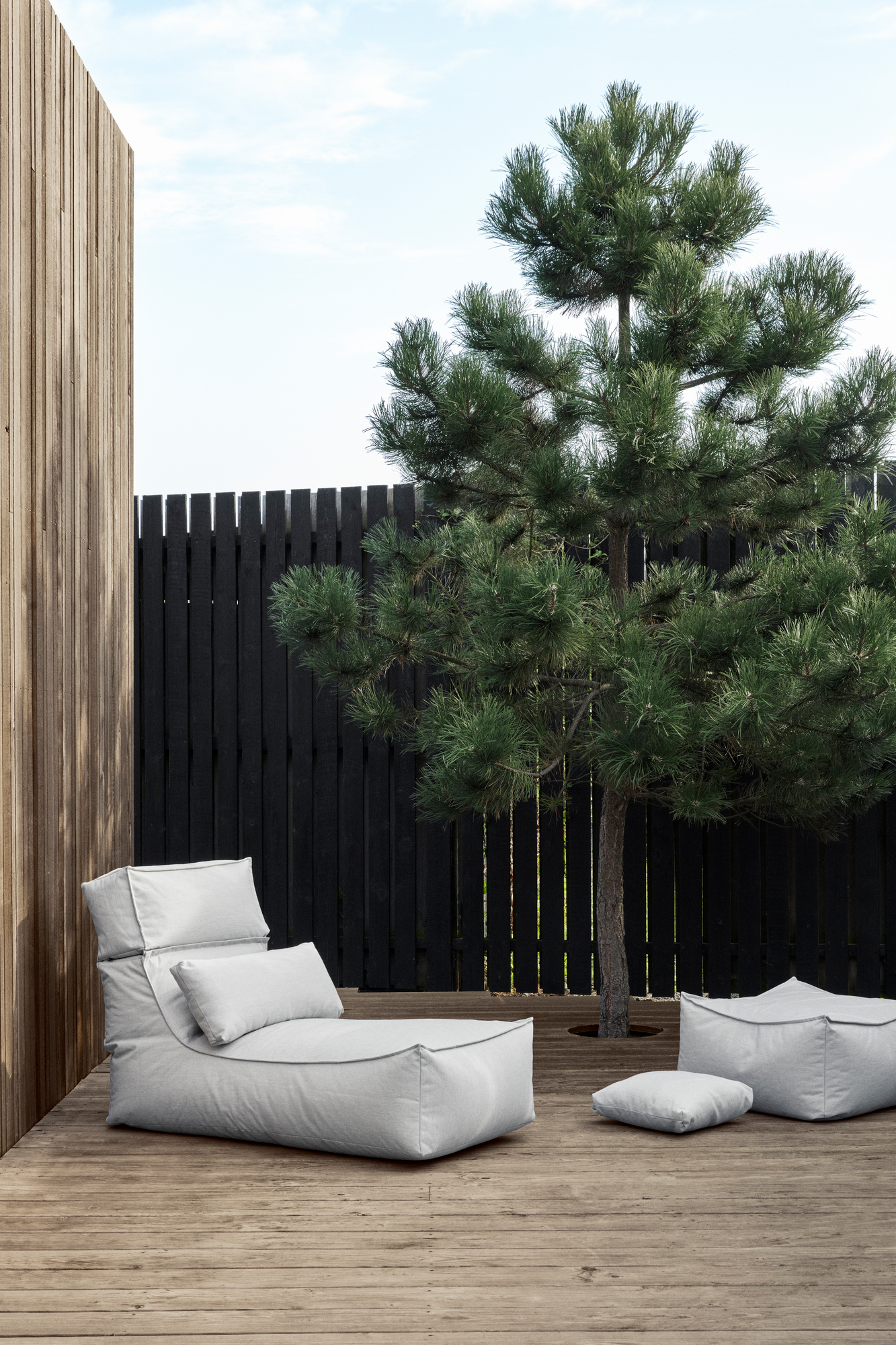Blomus STAY Outdoor Kissen Einzelstück, hellgraues Lounge-Kissen und Sitzwürfel auf Holzterrasse mit Baum.