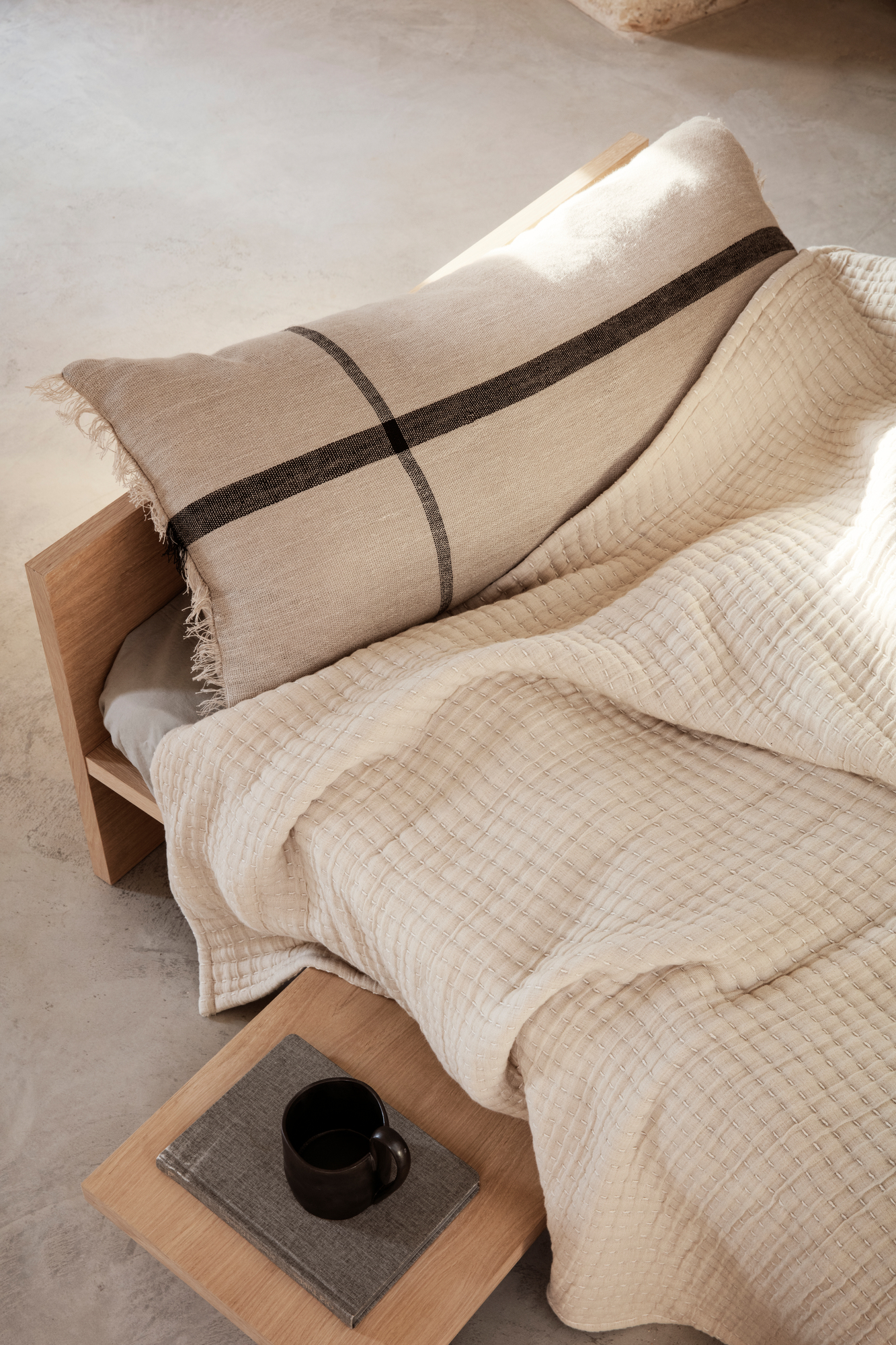 Detailaufnahme des Kona Bettes von Ferm Living mit Decke, Kissen und Nachttisch.