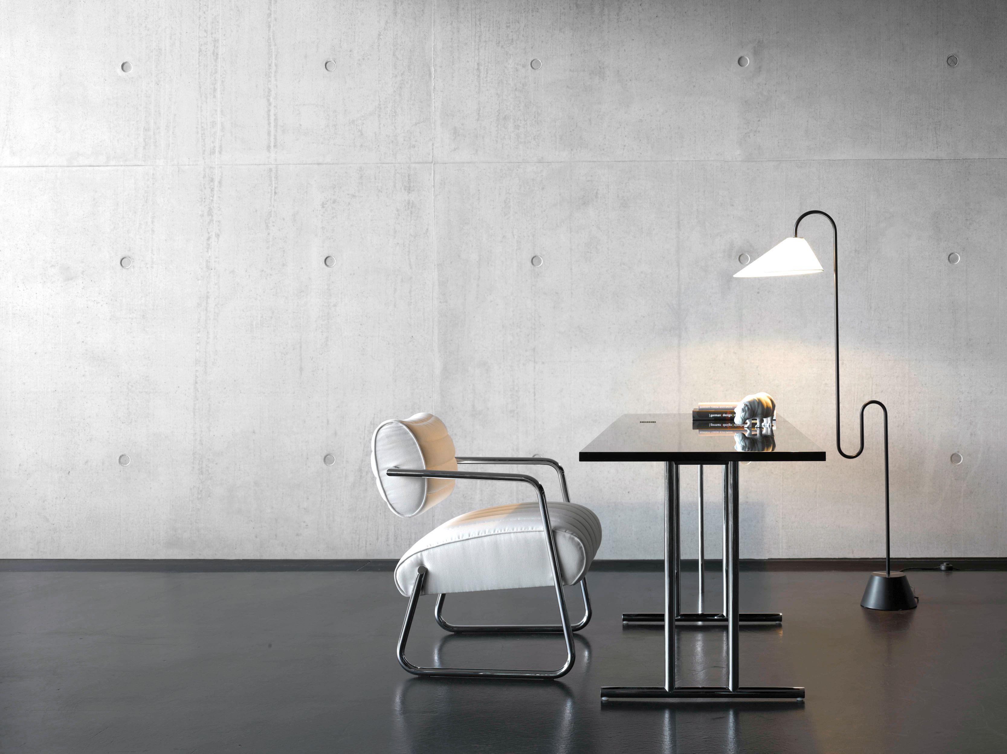 Lou Perou Ausklapptisch von ClassiCon mit Lampe und Sessel vor einer Betonwand, modernes Bürodesign.