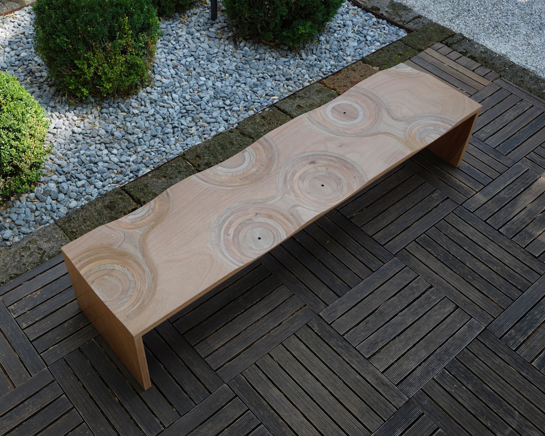Casamania Horm Ripples Bank für den Außenbereich aus hellem Holz mit kreisförmigem Muster.