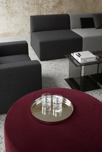 SF06 Kerman Modulsofa von e15 in Grau, kombiniert mit rotem Hocker und Glasbeistelltisch.