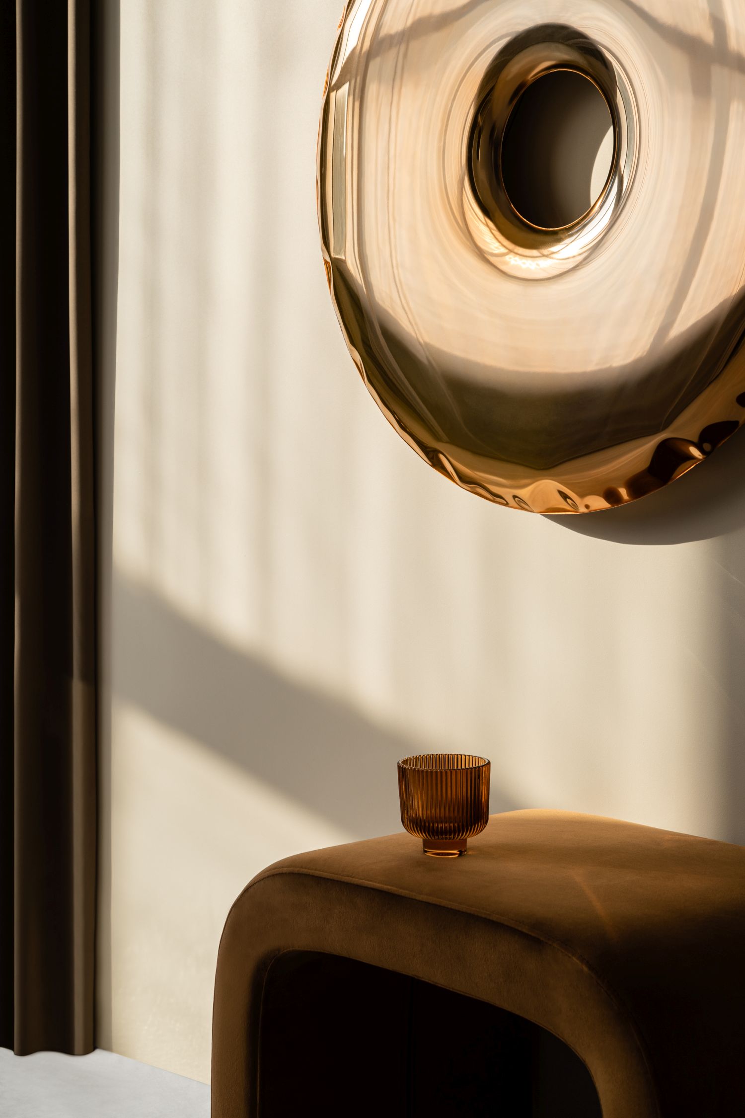 Nahaufnahme des Rondo Spiegels Aurum Gold von Zieta, montiert an einer Wand über einem braunen Hocker.