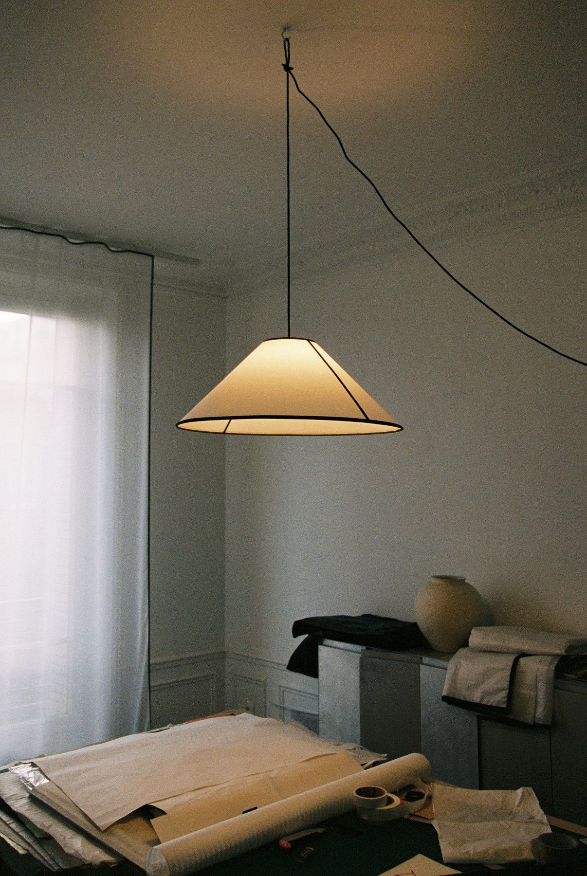 Nahaufnahme der stilvollen Ava Cone Pendelleuchte von Hay, die ein warmes Licht in einem Arbeitszimmer spendet.