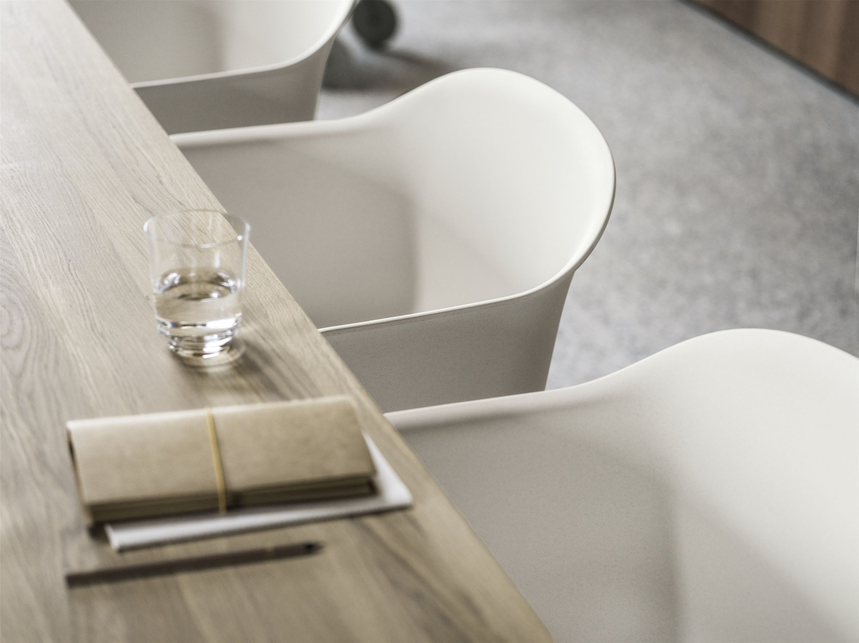 Nahaufnahme eines Muuto Fiber Armchair Stuhls mit Holzbeinen an einem Tisch mit Notizbuch.