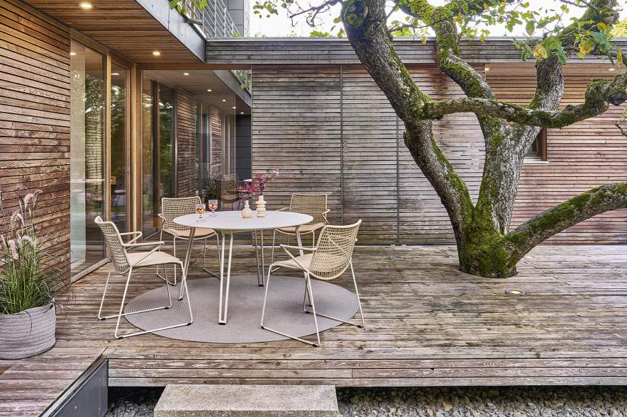 Weishäupl Slope Tisch, runder Esstisch für den Außenbereich auf einer Holzterrasse mit Stühlen.