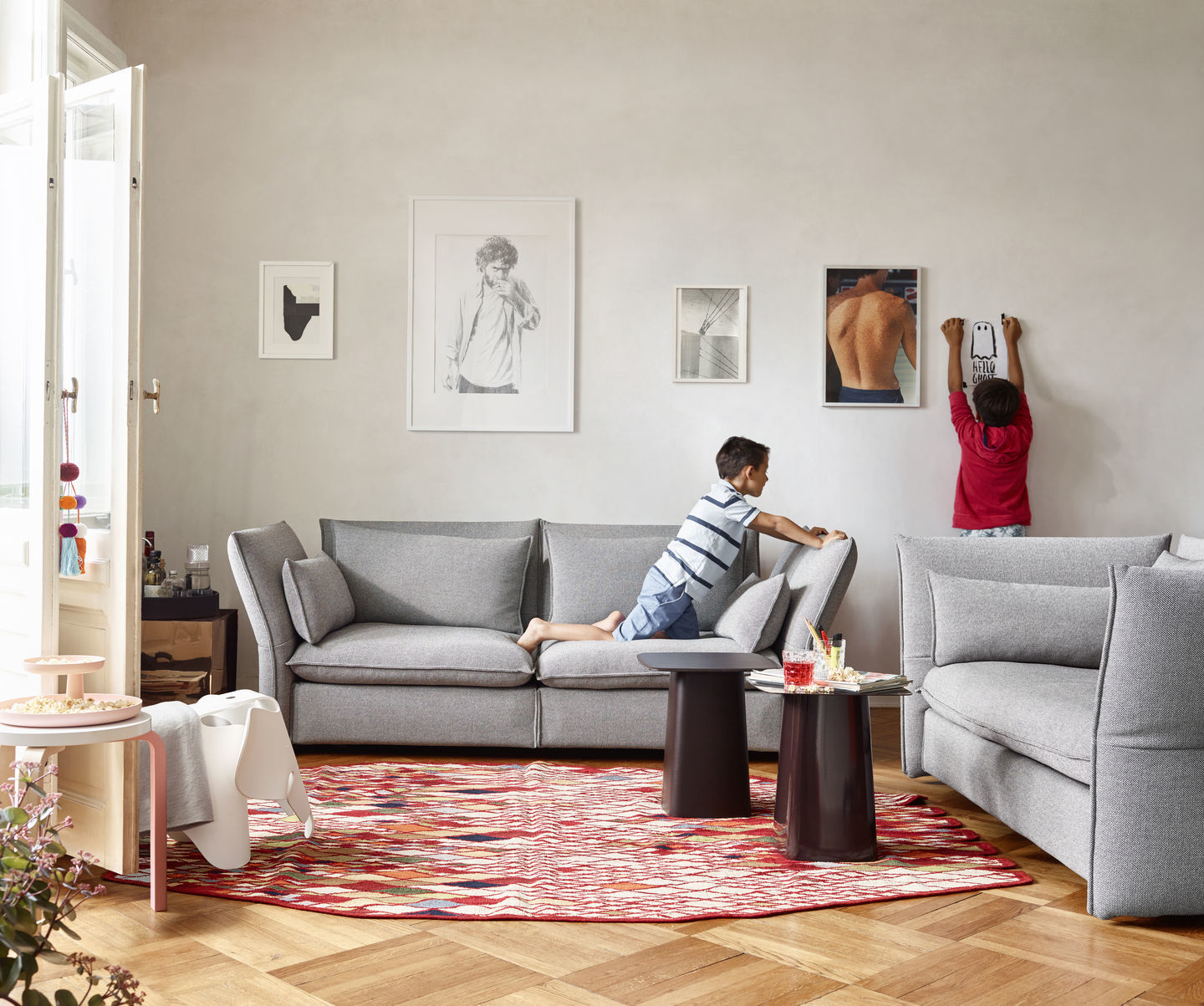 Wohnzimmer mit grauem Sofa, rotem Teppich und zwei kleinen Vitra Beistelltischen aus Metall.