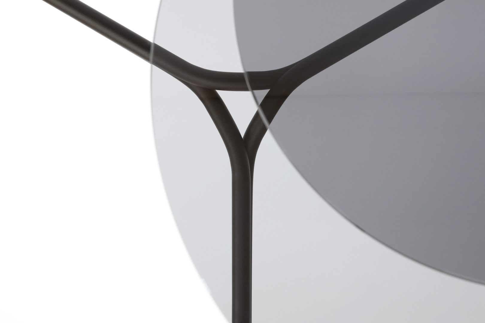 Detailaufnahme des transparenten Lej Couchtisches von Mox mit filigranem, dunklem Metallgestell und runder Glasplatte.