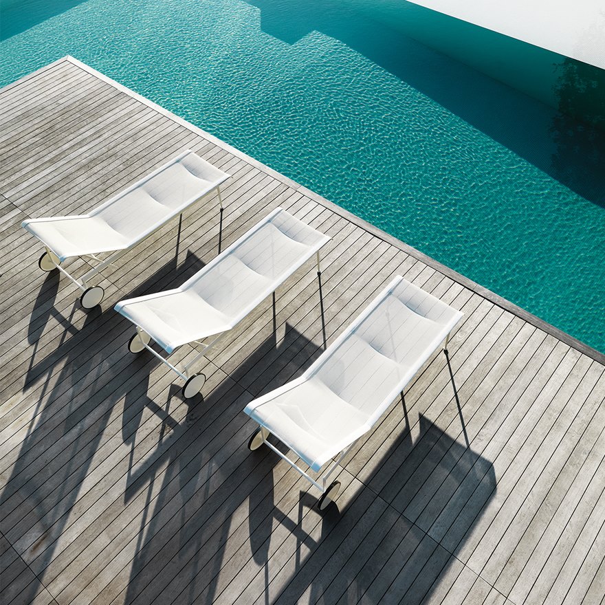 Drei weiße Richard Schultz Liegen auf Holzdeck neben einem Pool. Outdoor Möbel.