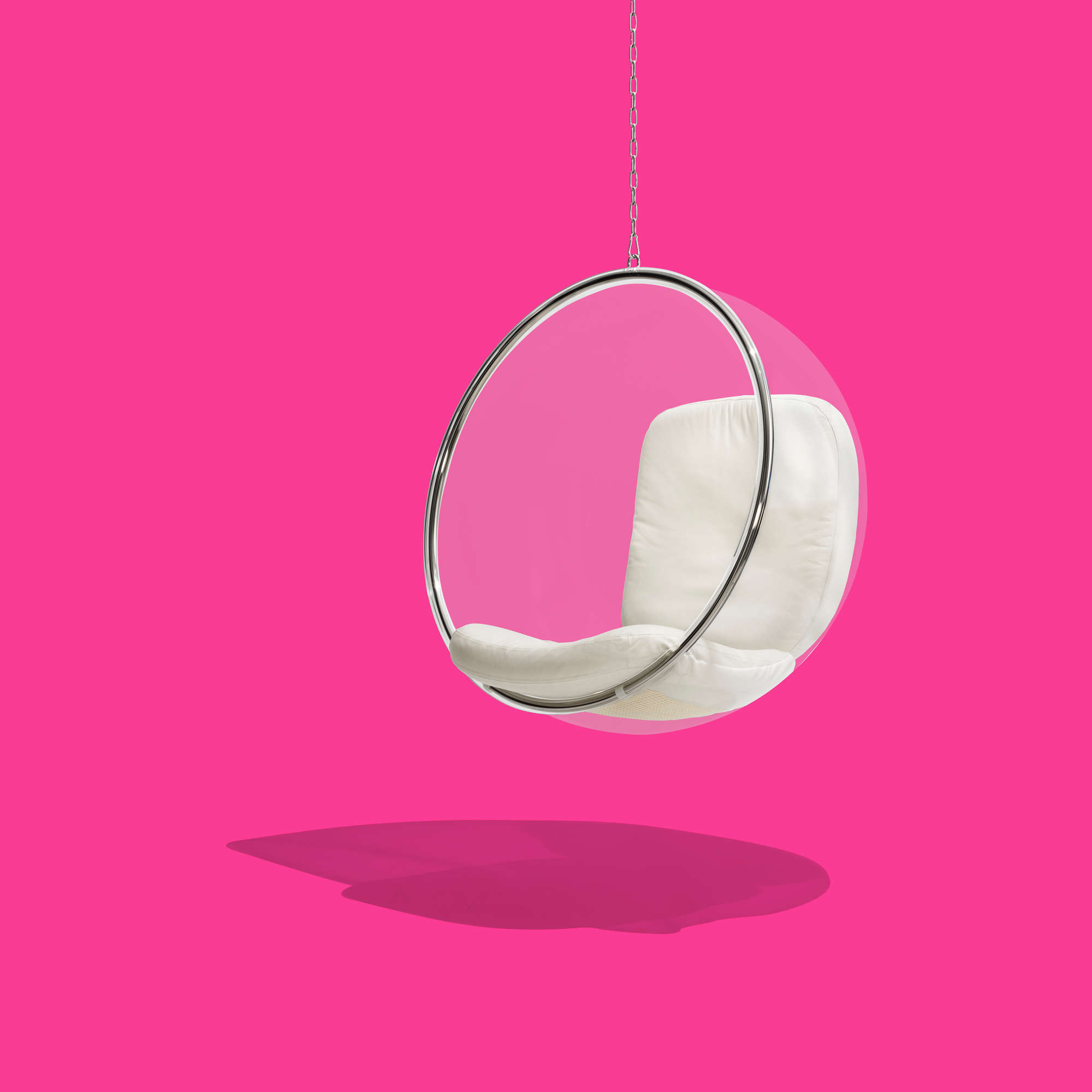Bubble Chair: Transparenter Hängesessel mit weißen Kissen, aufgehängt an einer Kette vor pinkfarbenem Hintergrund.