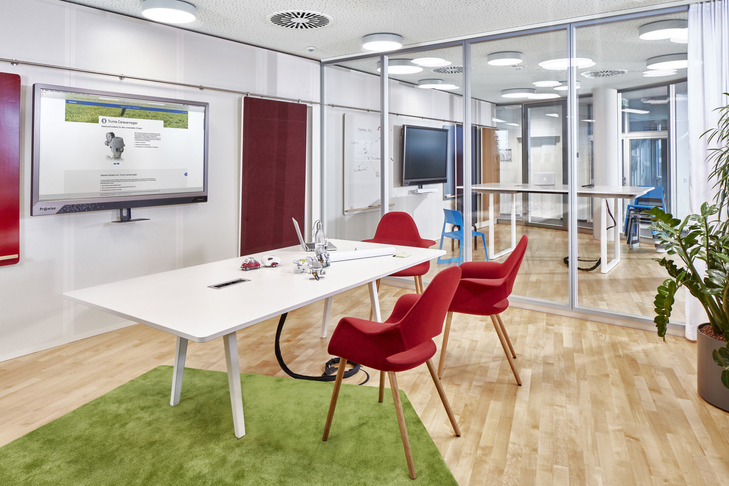Konferenzraum mit weißem Tisch, grünen Teppich und roten Organic Conference Stühlen von Vitra.