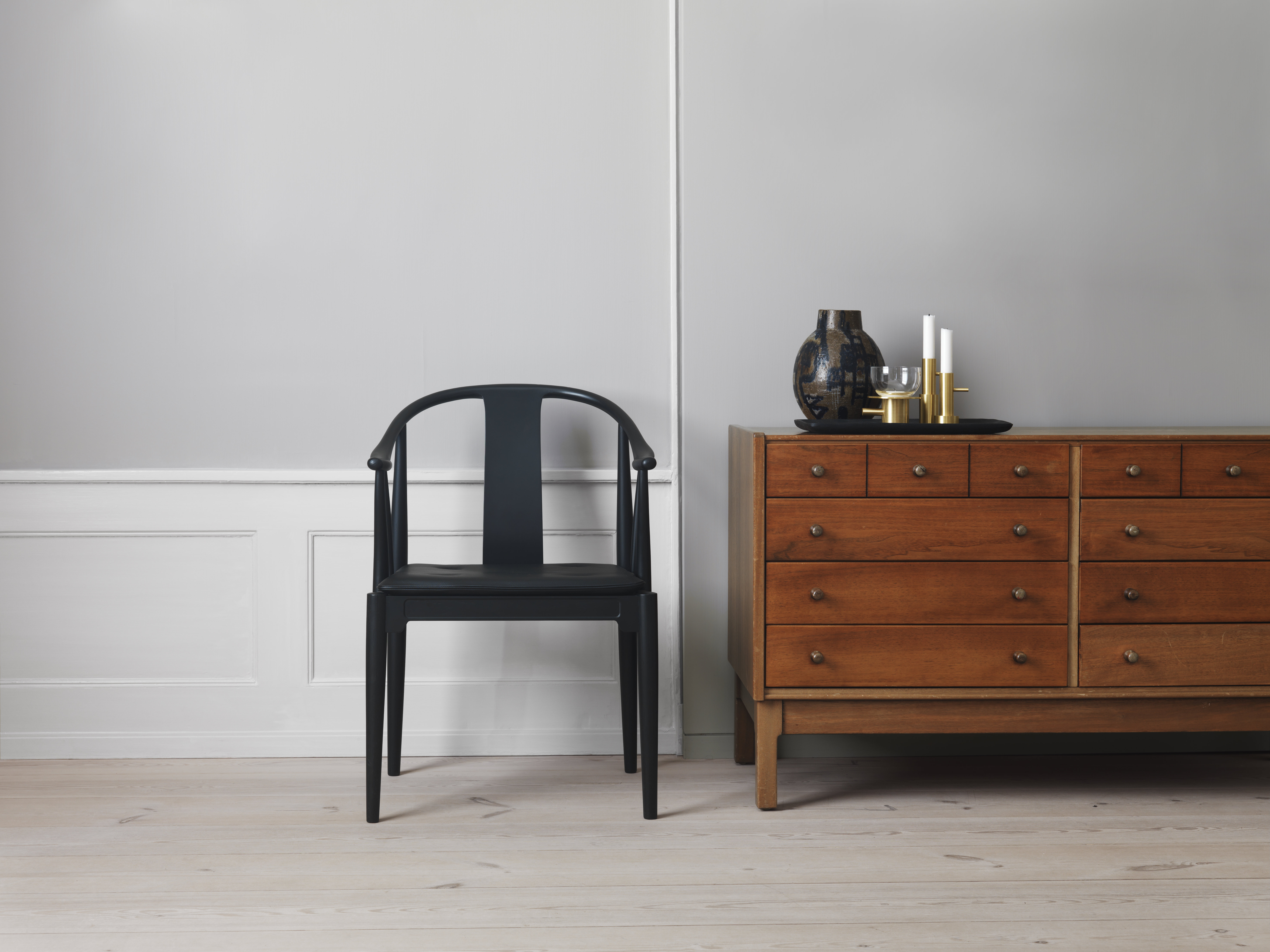 Schwarzer China Chair Stuhl von Fritz Hansen neben einer Holzkommode mit dekorativen Wohnaccessoires.