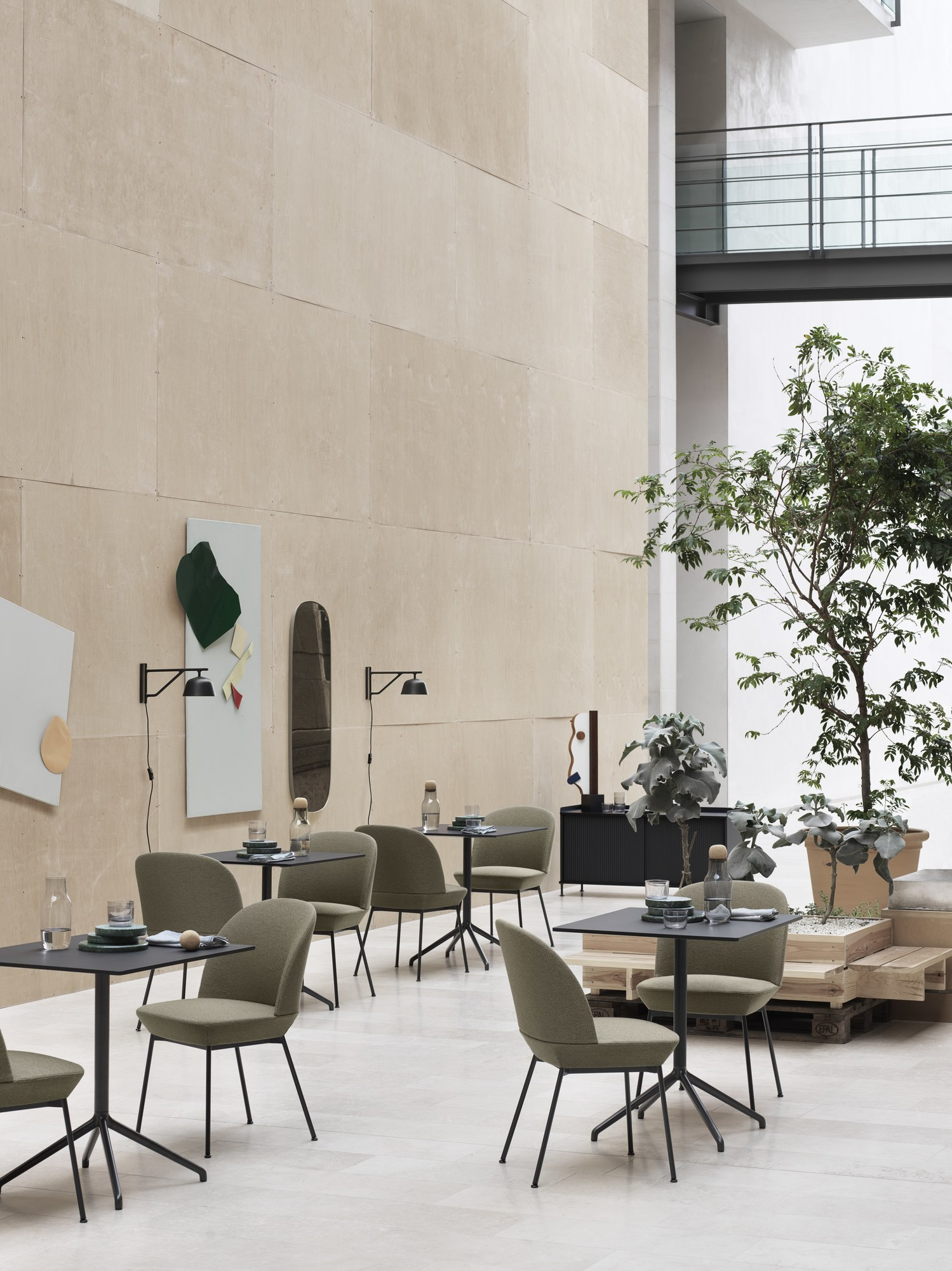 Innenraum mit Tischen, Stühlen und zwei schwarzen Ambit Wandleuchten von Muuto an der Wand.