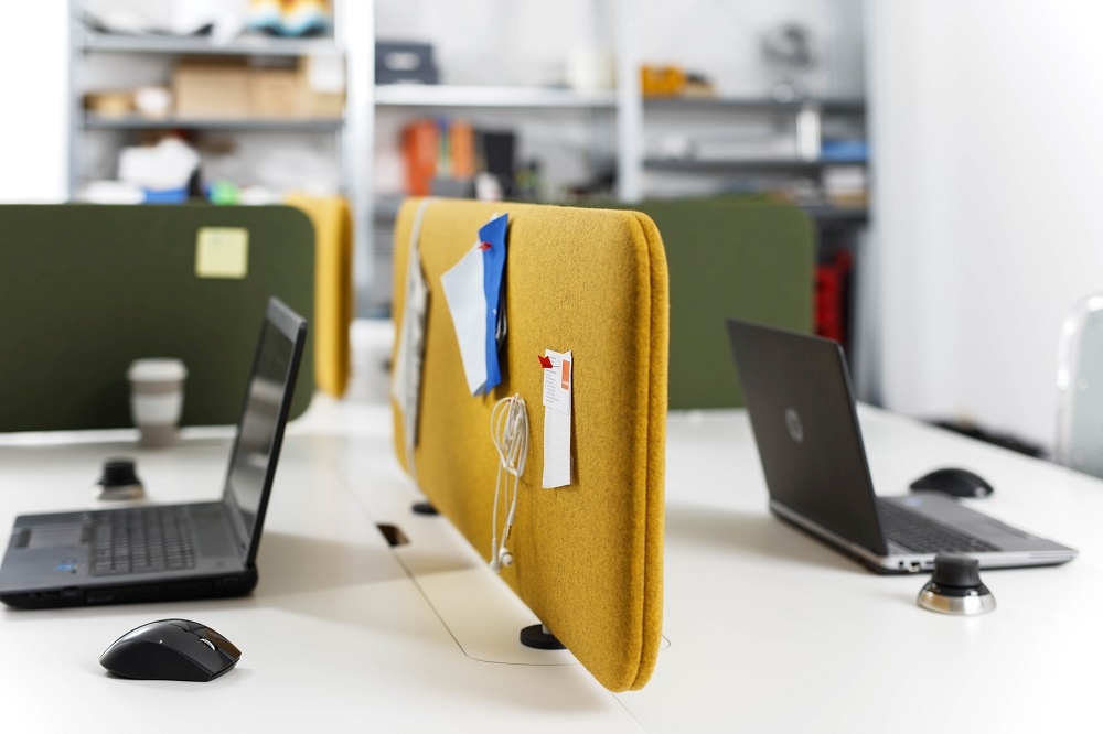 Gelbes Cascando Pillow Desk Akustikelement auf einem Schreibtisch mit Laptop und Büroartikeln. Schallschutz für Büro.