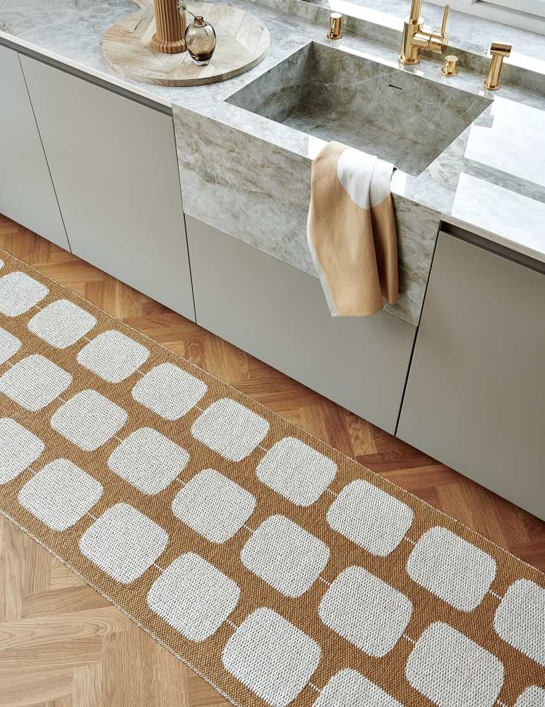 Pappelina Sten Kunststoffteppich 70x200 cm in Braun-Weiß vor einer modernen Küchenzeile mit Holzboden.