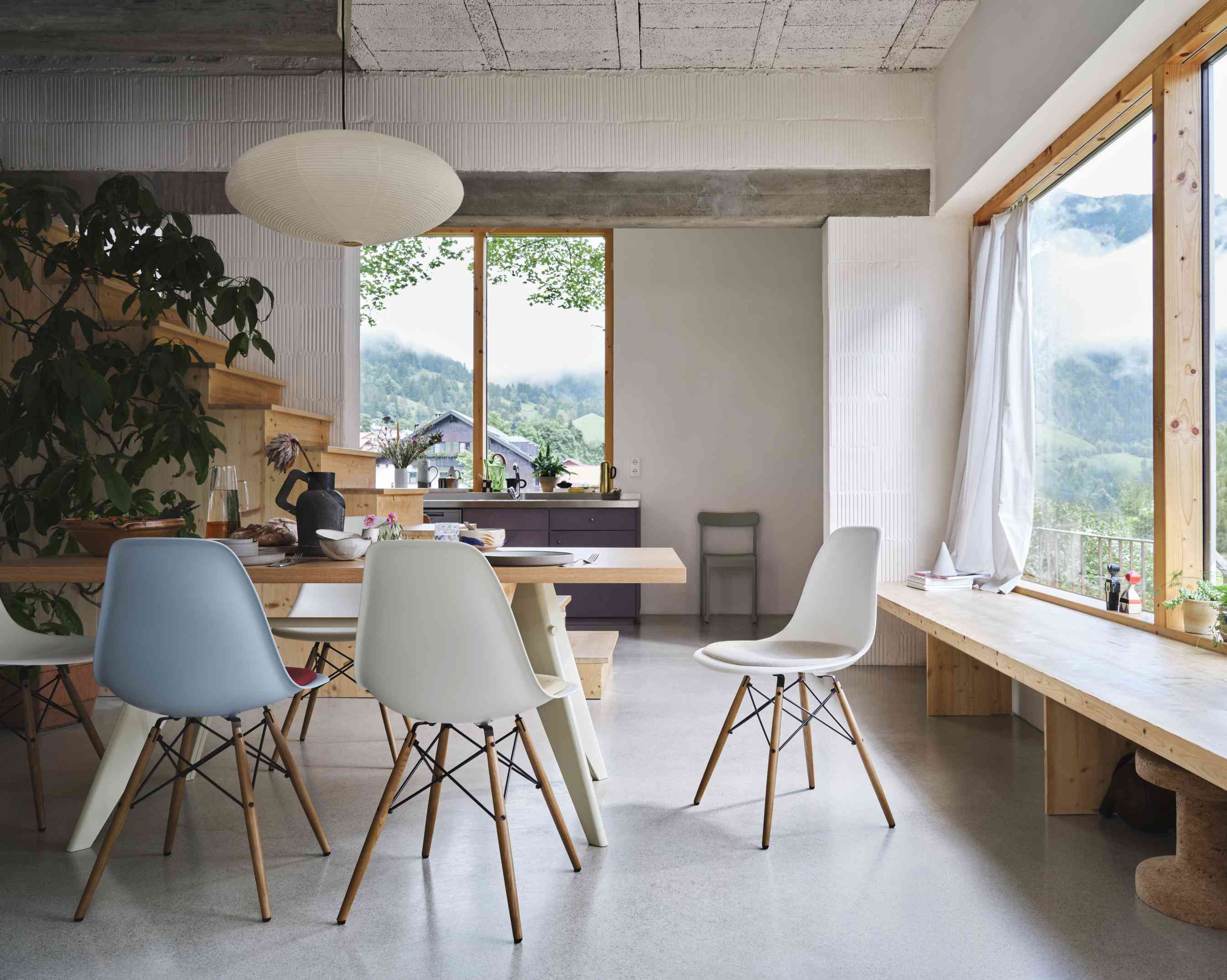 Esszimmer mit Holztisch und verschiedenen Vitra DSW Eames Plastic Chairs, Blick auf die Berge durch das Fenster.
