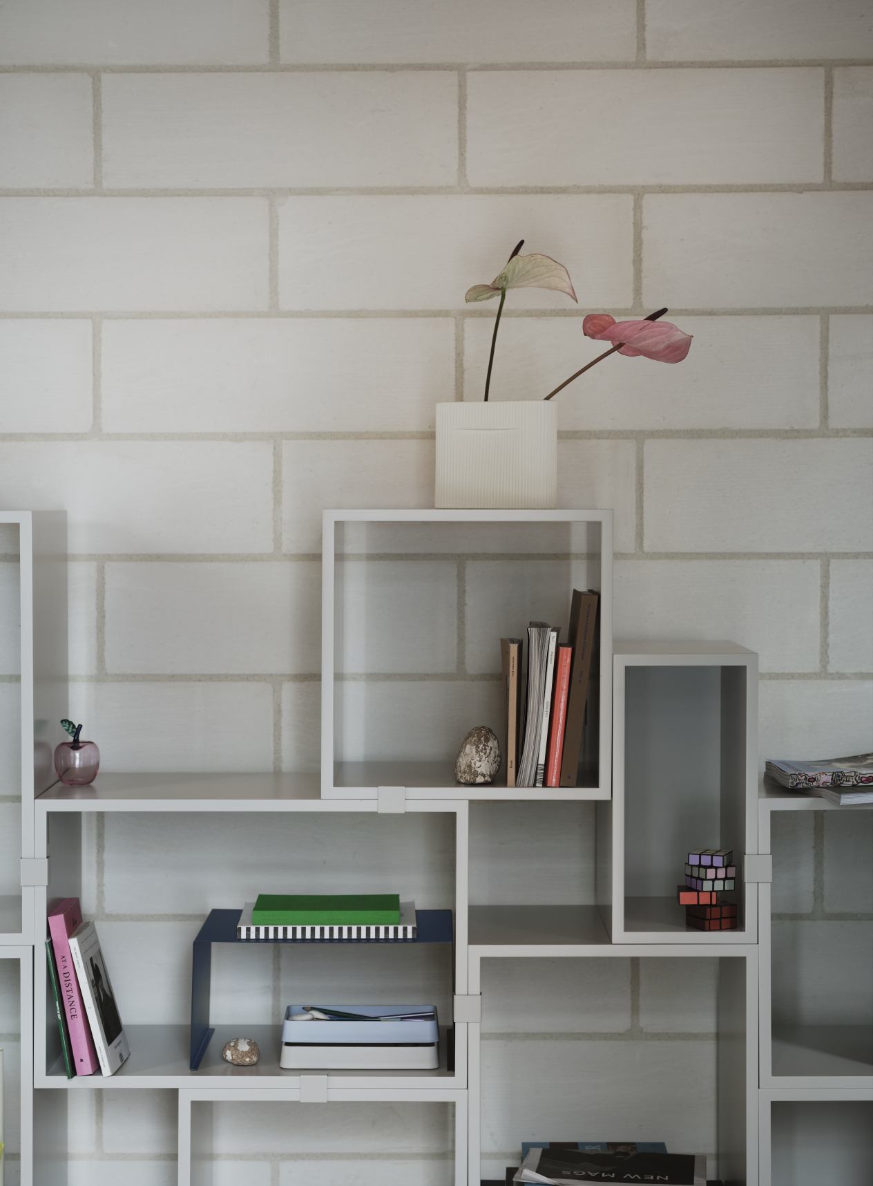 Weißes Muuto Stacked Storage Regalsystem 2.0 mit Deko vor einer weißen Ziegelwand. Modernes Regalsystem für Wohnzimmer.