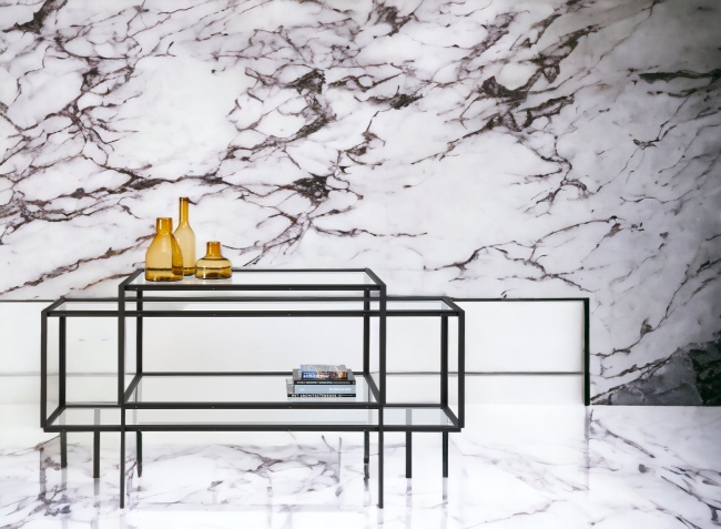 Tangled Kabinettschrank Sideboard Spectrum mit Glasablagen und schwarzem Metallgestell vor Marmorwand.