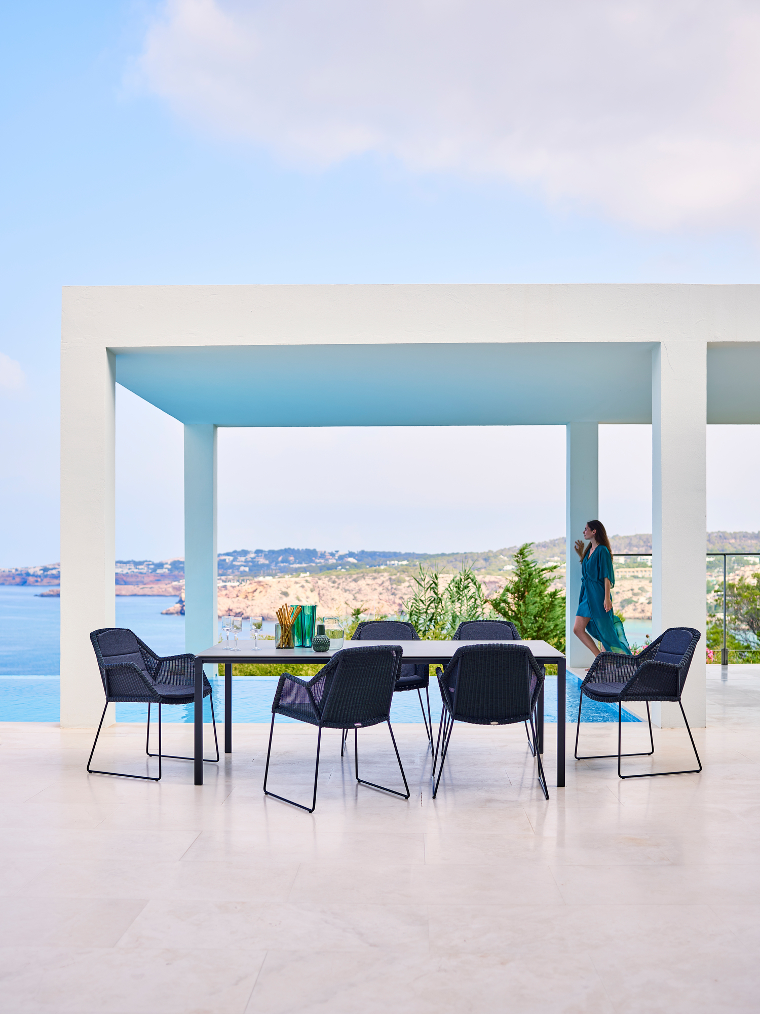 Cane-Line Esstisch Pure Outdoor mit schwarzen Stühlen auf einer Terrasse mit Meerblick.