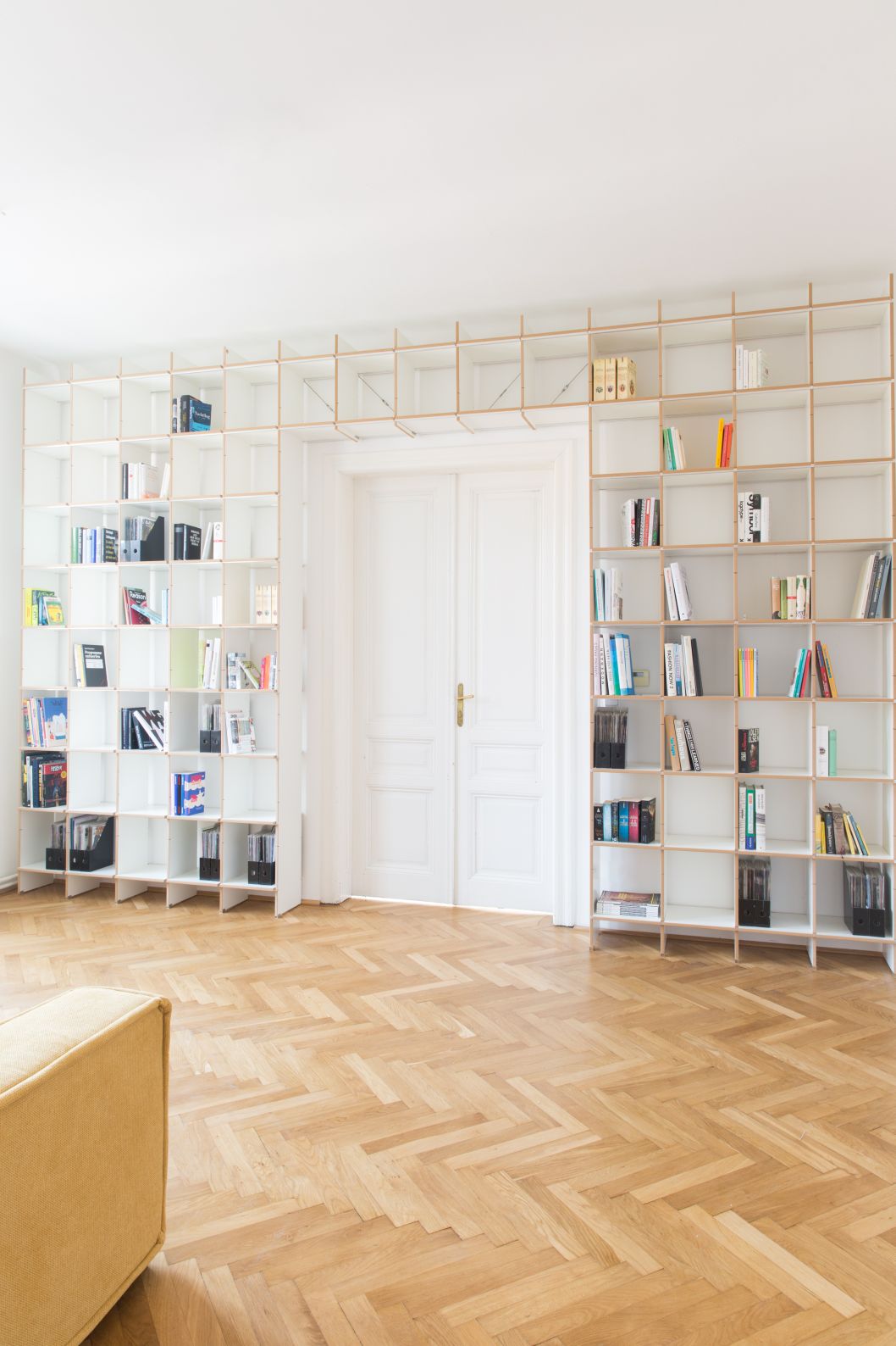 Großes, weißes modulares Bücherregal-System aus Holz, gefüllt mit Büchern und Ordnern, vor einer weißen Doppeltür.