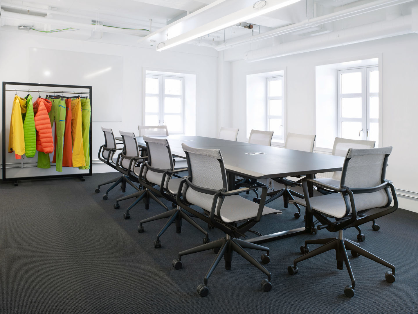 Physix Bürodrehstuhl von Vitra in einem hellen Konferenzraum mit schwarzem Tisch und bunten Jacken.