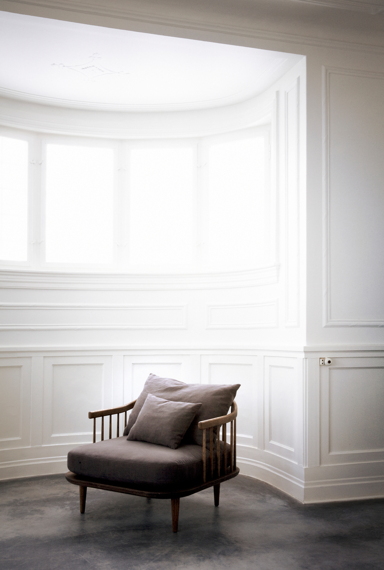 Fly Lounge Sessel von AndTradition, brauner Stoffbezug und Holzgestell, mit Kissen in hellem, modernem Raum.