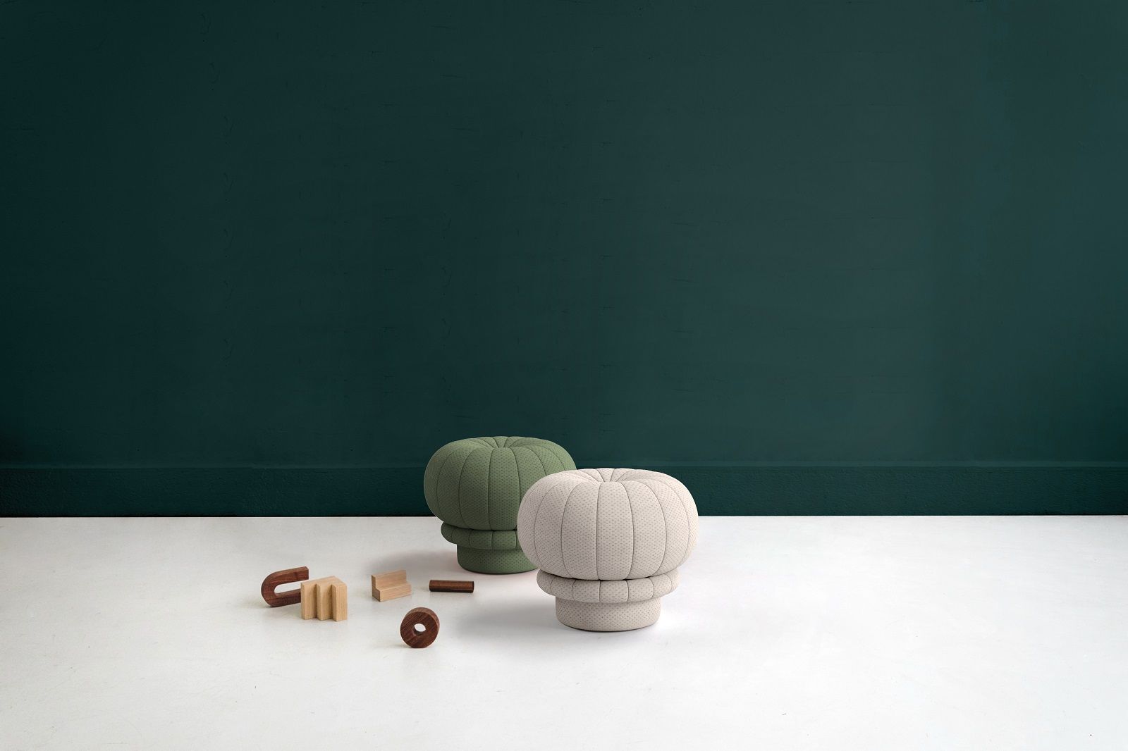 Zwei Claudie Pouf Hocker in Grün und Beige mit Holzspielzeug vor dunkelgrüner Wand.