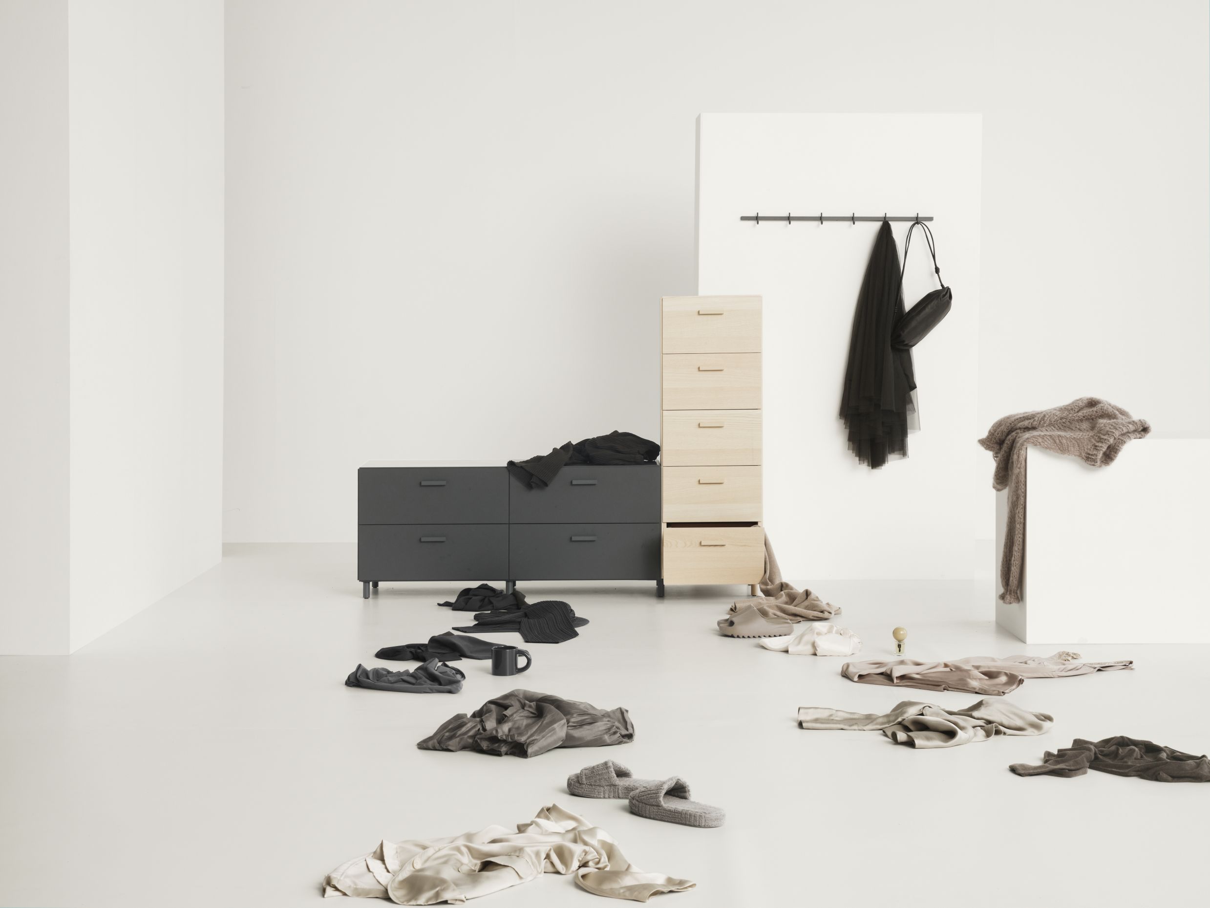 Graue Relief Hakenleiste von String Furniture an weißer Wand mit Kleidung und Accessoires.