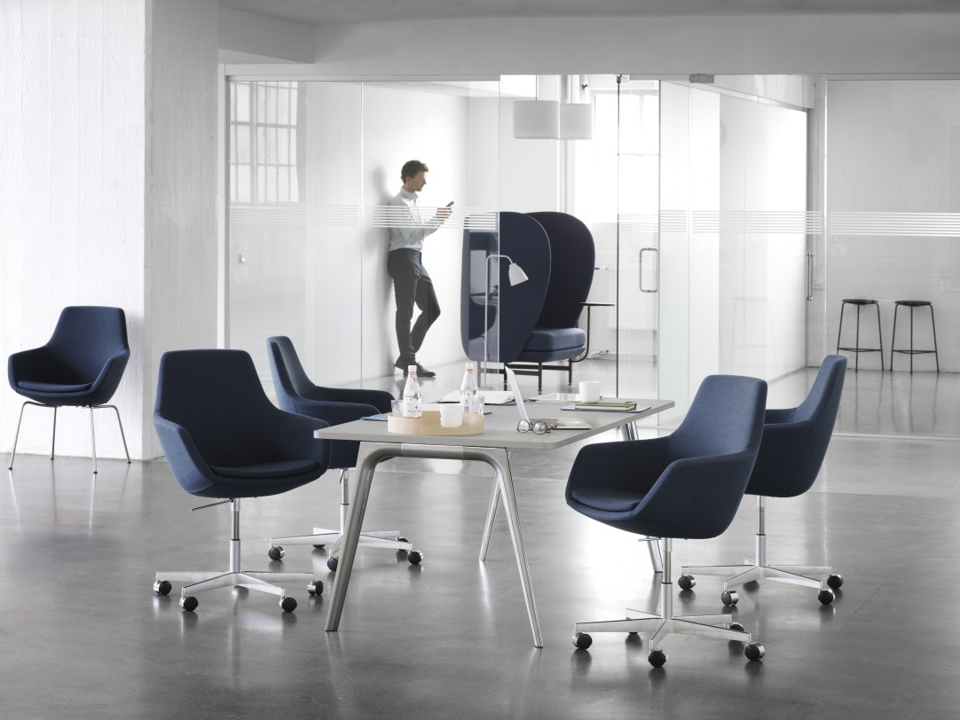 Innenraum mit Fritz Hansen Büromöbeln: Blaue Drehstühle mit Armlehne und Caravaggio Pendelleuchten über einem Konferenztisch.