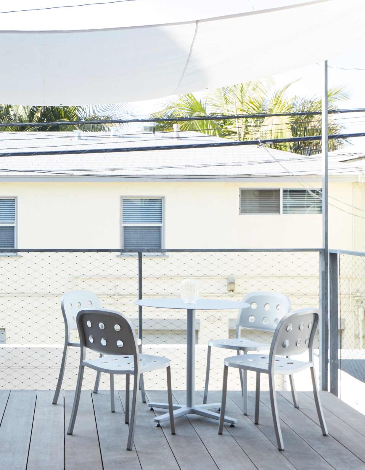 Vier graue Emeco 1 Inch Aluminium Stühle mit Löchern auf einem Balkon mit Tisch und Sonnensegel.