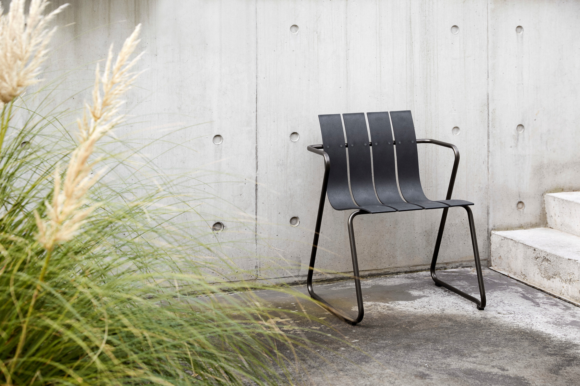 Schwarzer Ocean Chair Outdoor Stuhl von Mater vor einer Betonwand und Pampasgras.