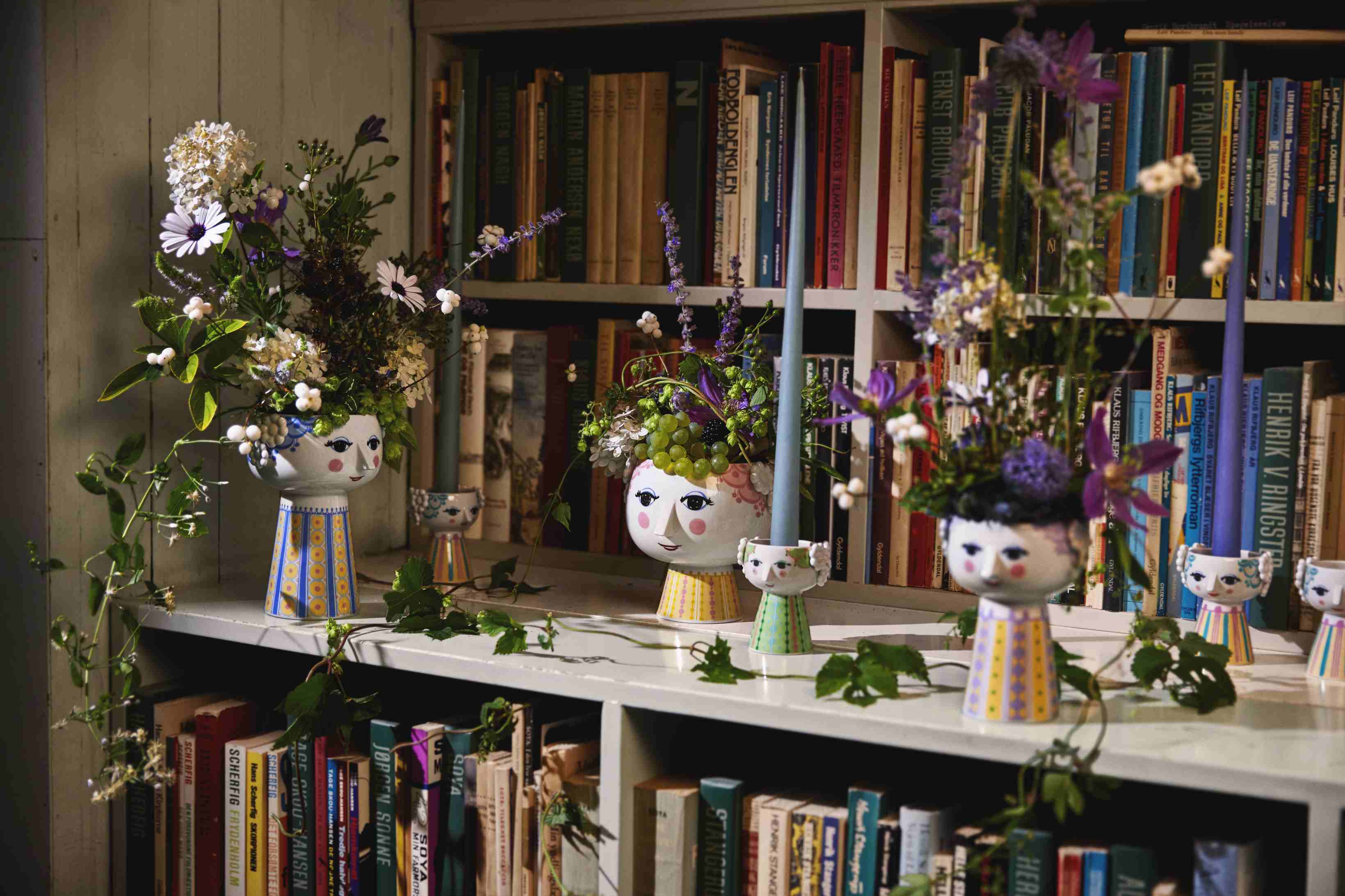 Verspielte Keramik: Vasen und Kerzenständer mit Gesichtern und Blumen vor Bücherregal, dekorative Wohnaccessoires für stilvolles Interieur.