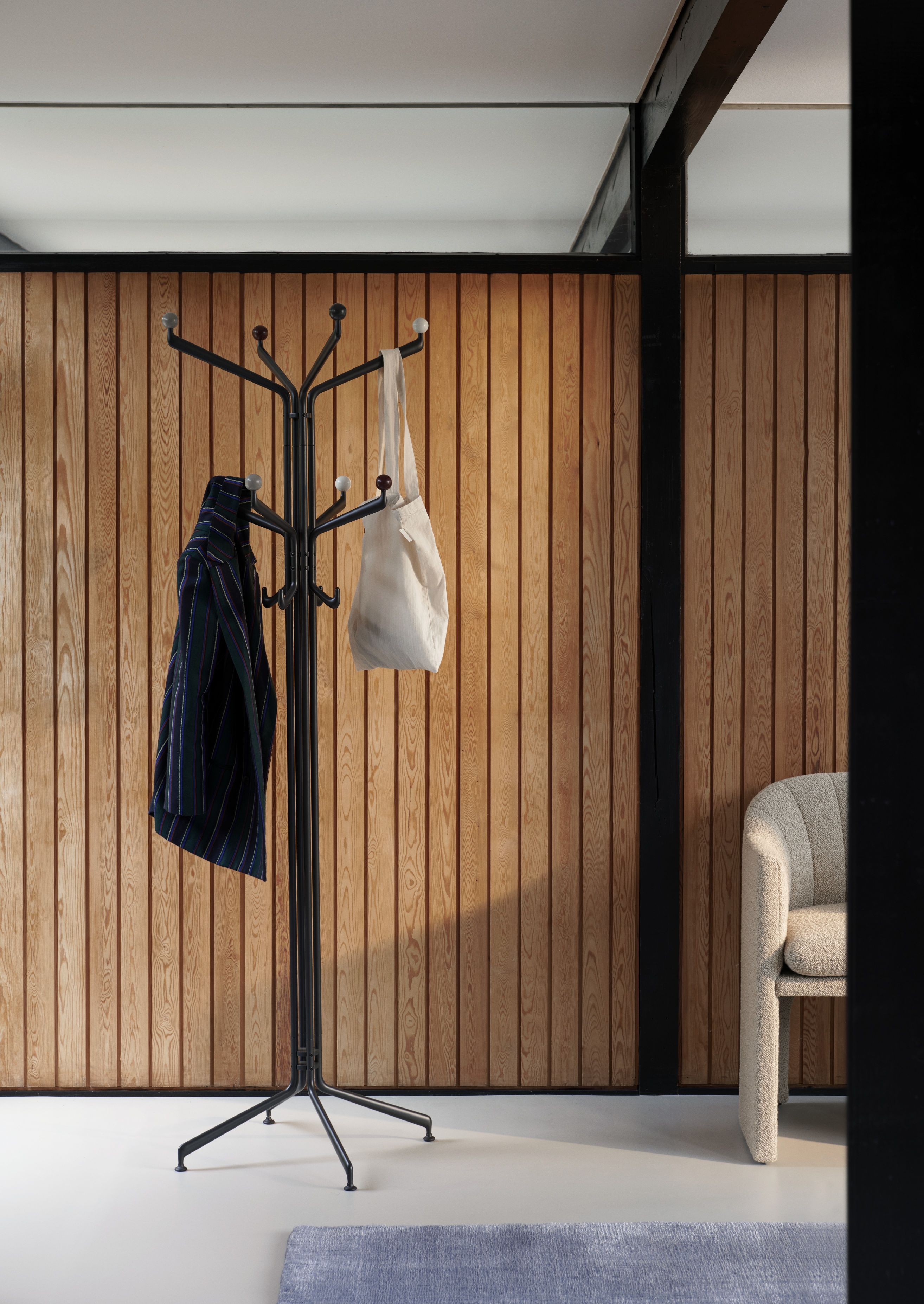 Capture SC77 Kleiderständer von AndTradition mit Jacke und Tasche vor einer Holzwand. Moderner Garderobenständer.