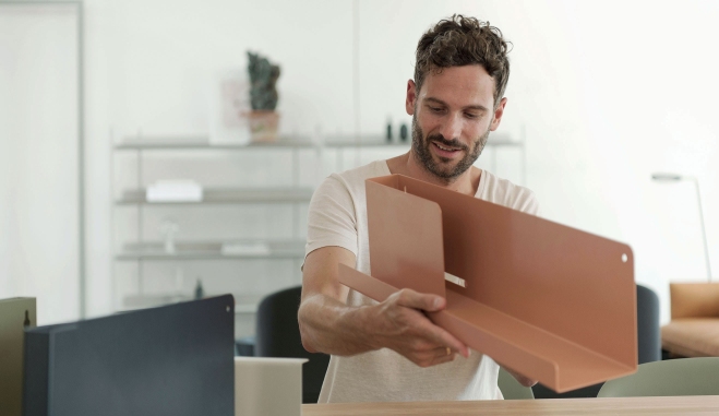 Mann hält ein Muuto Folded Shelves Regal in Kupferbraun, modernes Wandregal für Wohnzimmer und Büro.