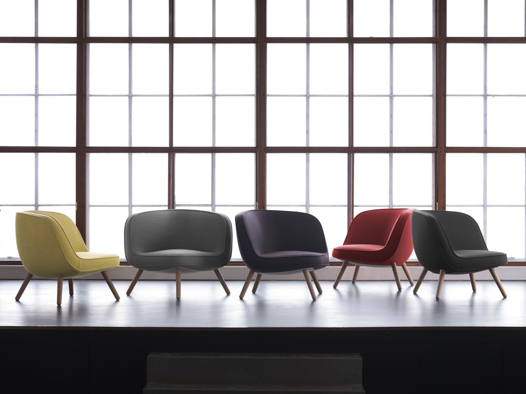 Fünf Fritz Hansen Sessel Via57 in Gelb, Grau, Lila, Rot und Schwarz vor einem Fenster.
