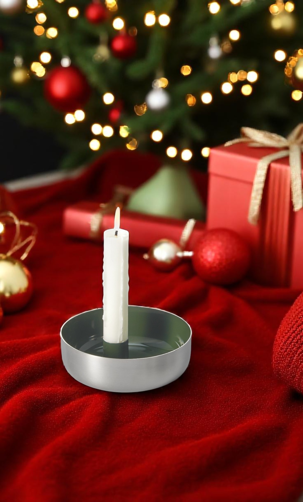 Brennende weiße Kerze in Biel Kerzenschale von Philippi aus Stahl vor Weihnachtsdekoration auf rotem Stoff.