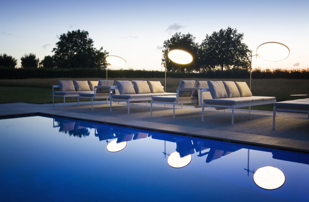 Sol + Luna Outdoor-Sofa-Sonnenliegen von Extremis neben Pool mit reflektierenden Lampen im Garten bei Dämmerung.