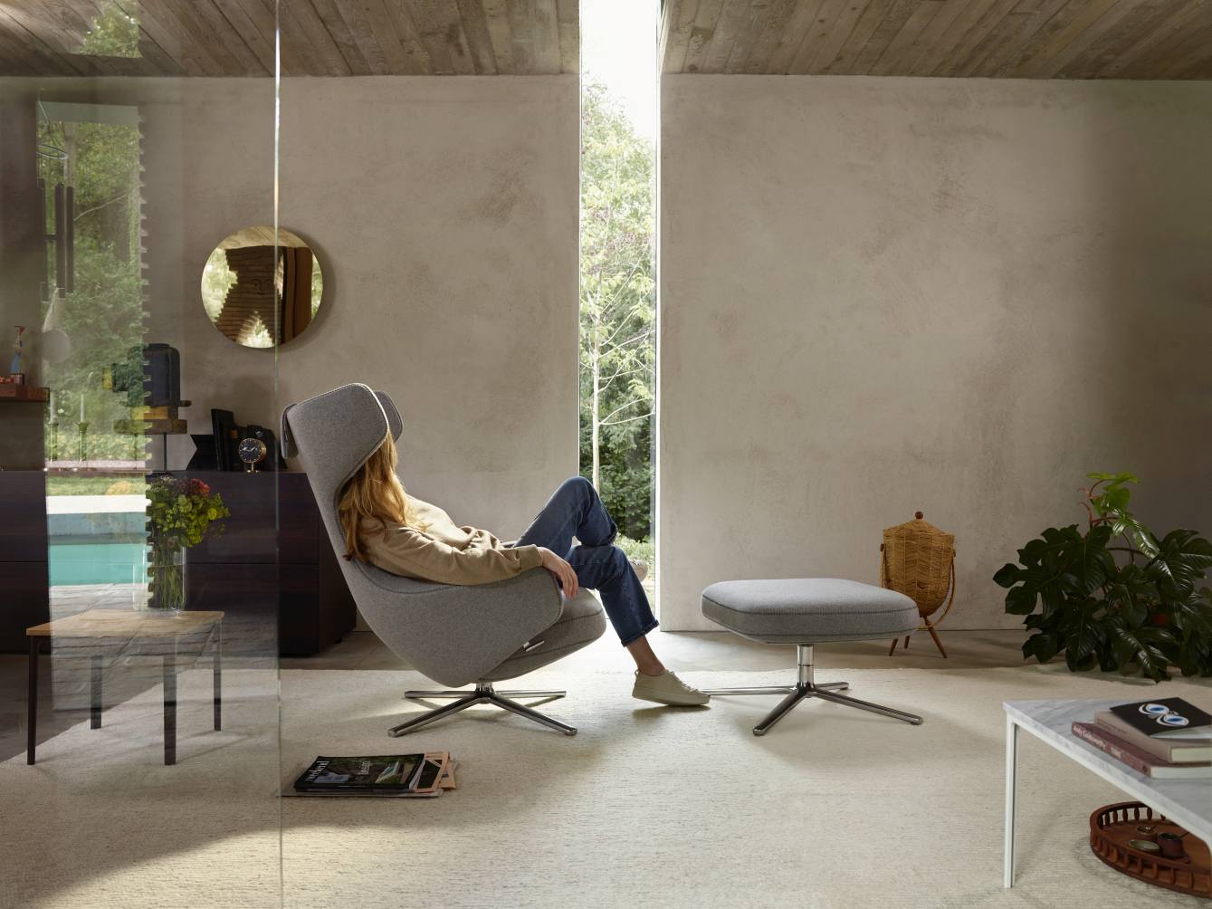 Frau entspannt im grauen Grand Repos Sessel mit Ottoman von Vitra in modernem Wohnzimmer.