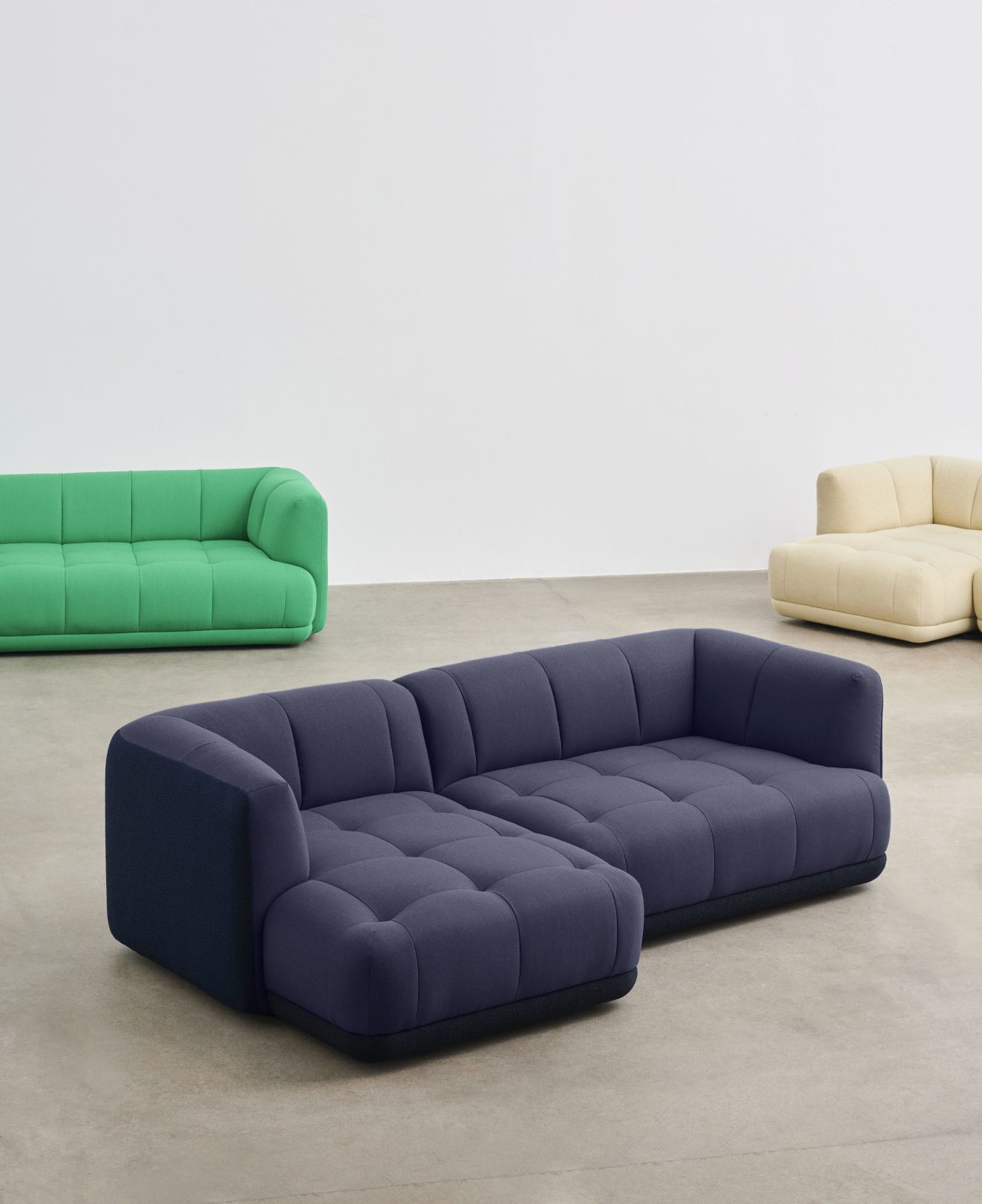 Blaues Quilton Sofa von Hay mit Chaiselongue und weiteren Sofas in Grün und Beige.