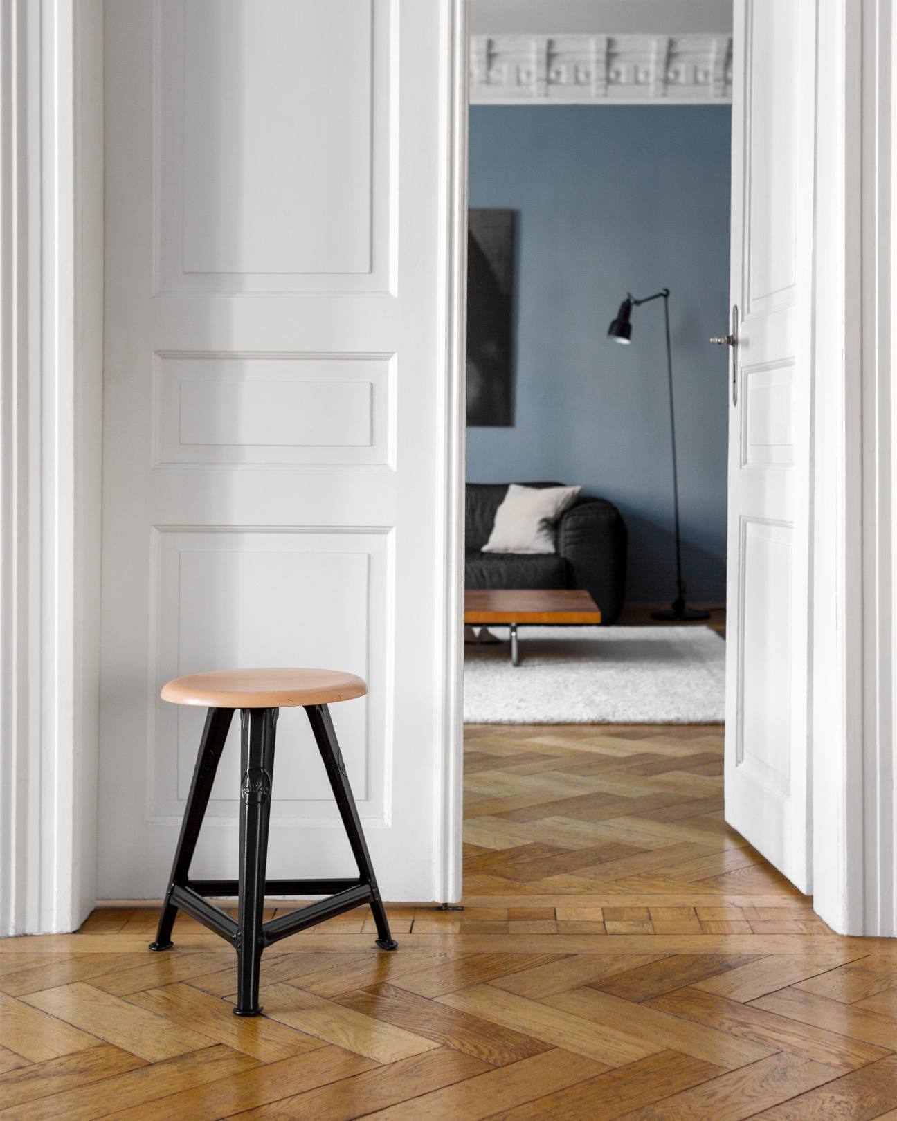 Rowac Schemel Model I 50 cm Hocker aus Holz und Stahl vor weißer Tür.
