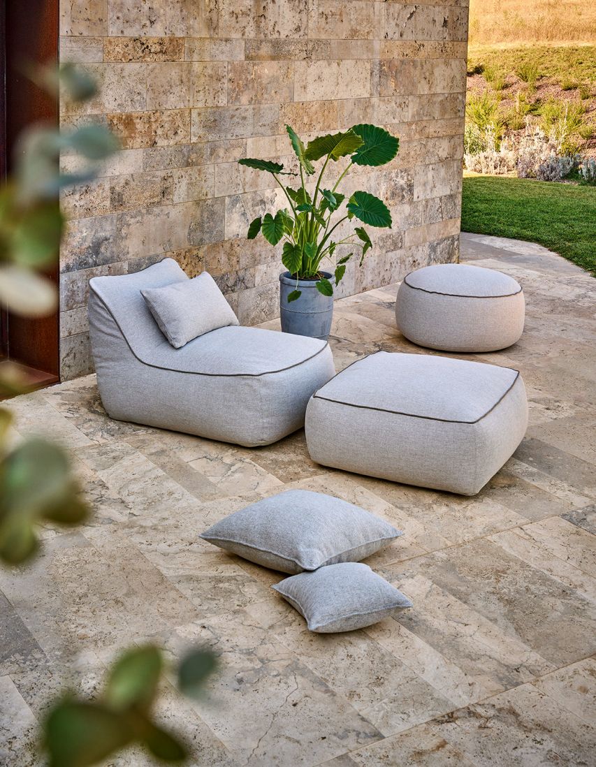 Maliha Lounge Sessel Outdoor Weishäupl Pebble mit Ottoman und Kissen auf einer Terrasse.