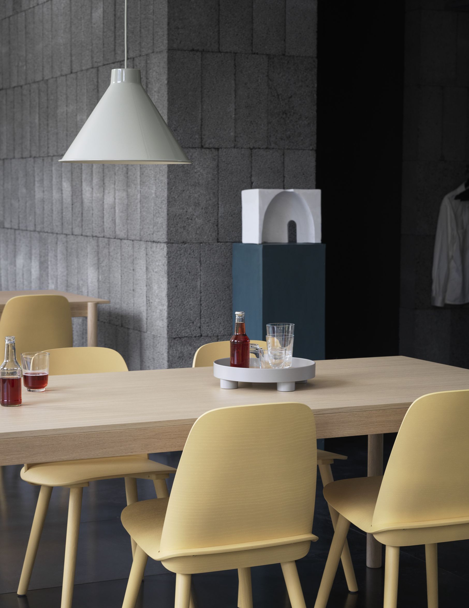 Helle Muuto Pendelleuchte über Esstisch mit gelben Stühlen und Getränken, modernes skandinavisches Design.