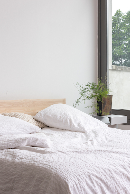 Nahaufnahme eines ZIANS Bettes Large mit hellem Holzrahmen, weißen Kissen und Bettwäsche in einem hellen Schlafzimmer.