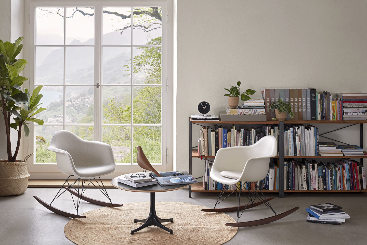 Zwei Eames RAR Schaukelstühle von Vitra in Weiß und Ahorn vor Fenster und Bücherregal.