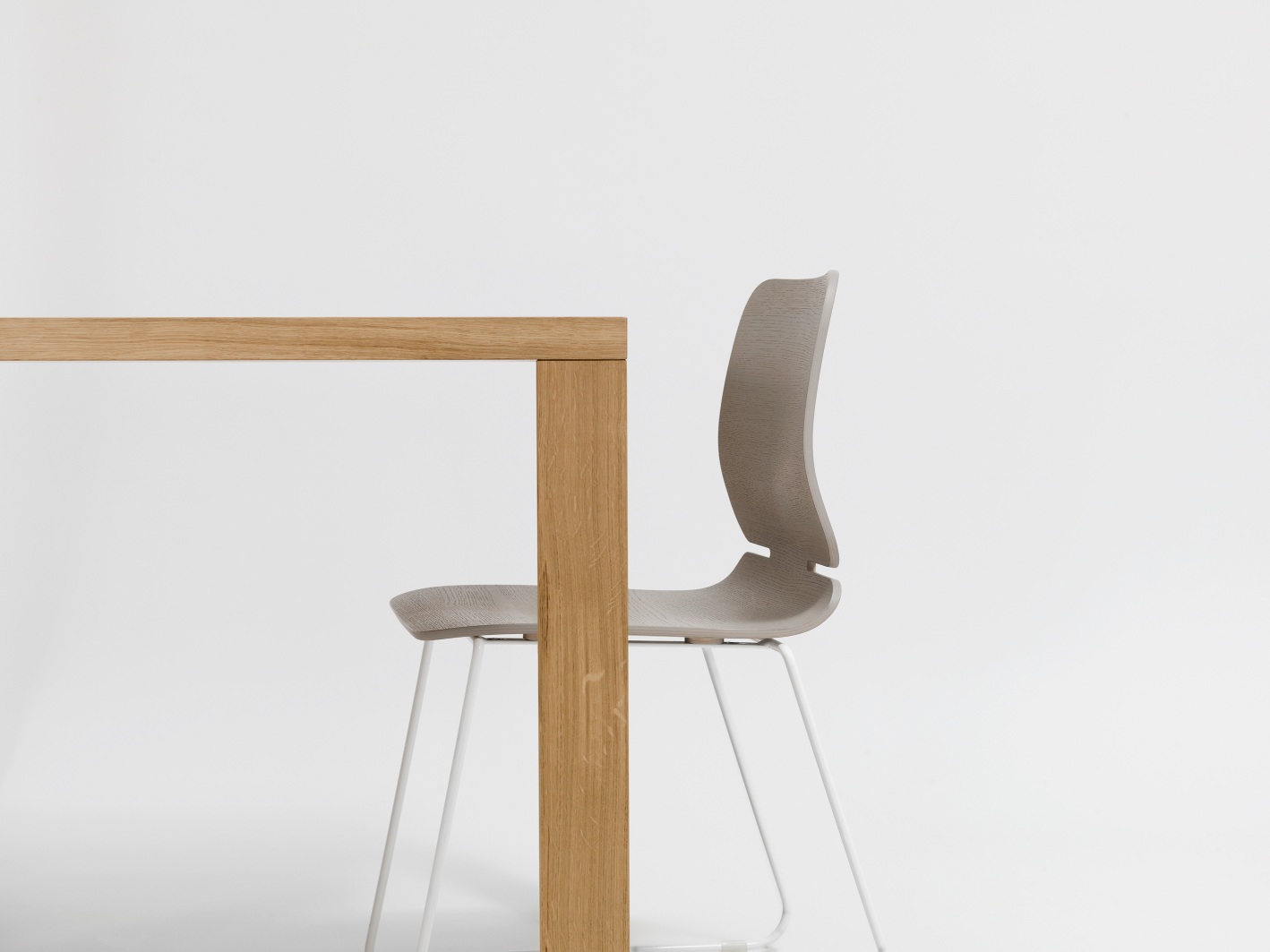 Detailaufnahme von Pjur Esstisch mit Stuhl: Moderner Holztisch und grauer Stuhl mit weißen Beinen vor hellem Hintergrund.