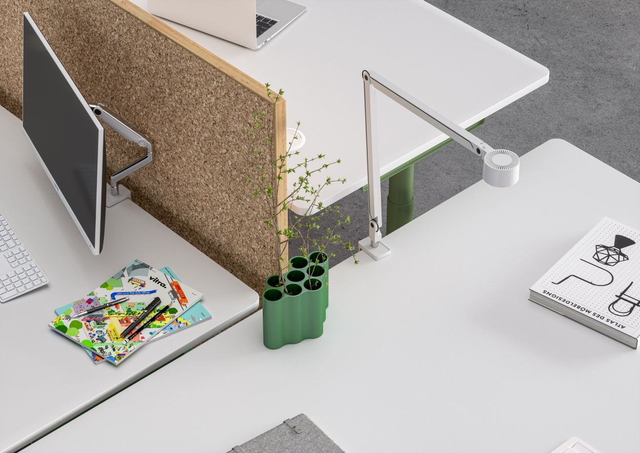 Detailaufnahme vom Vitra Tyde Steh- und Sitztisch mit Korkwand, Schreibtischlampe und Monitor für modernes Büro.