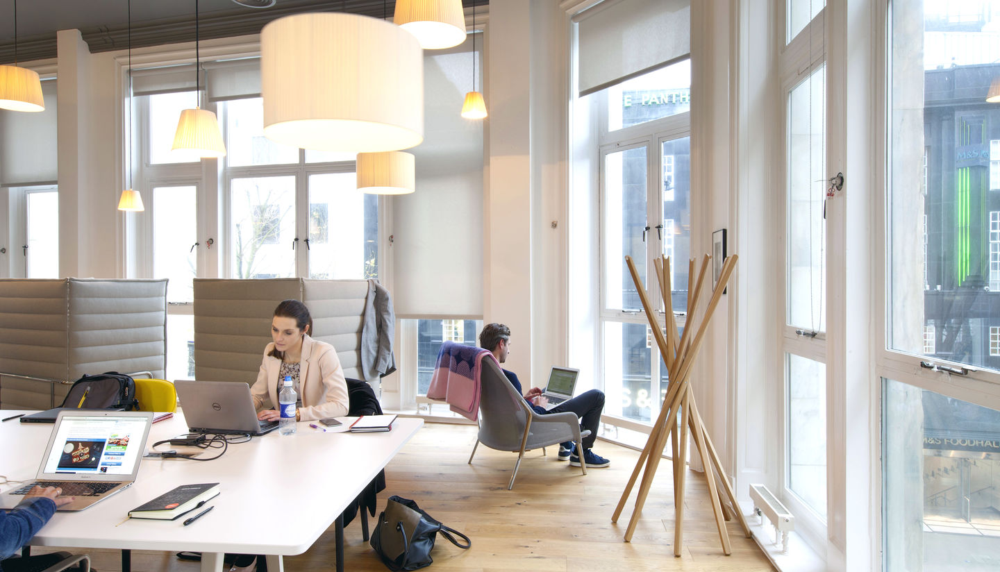 Heller Büroraum mit einer Person im grauen Vitra Slow Chair Sessel mit Ottoman beim Arbeiten.