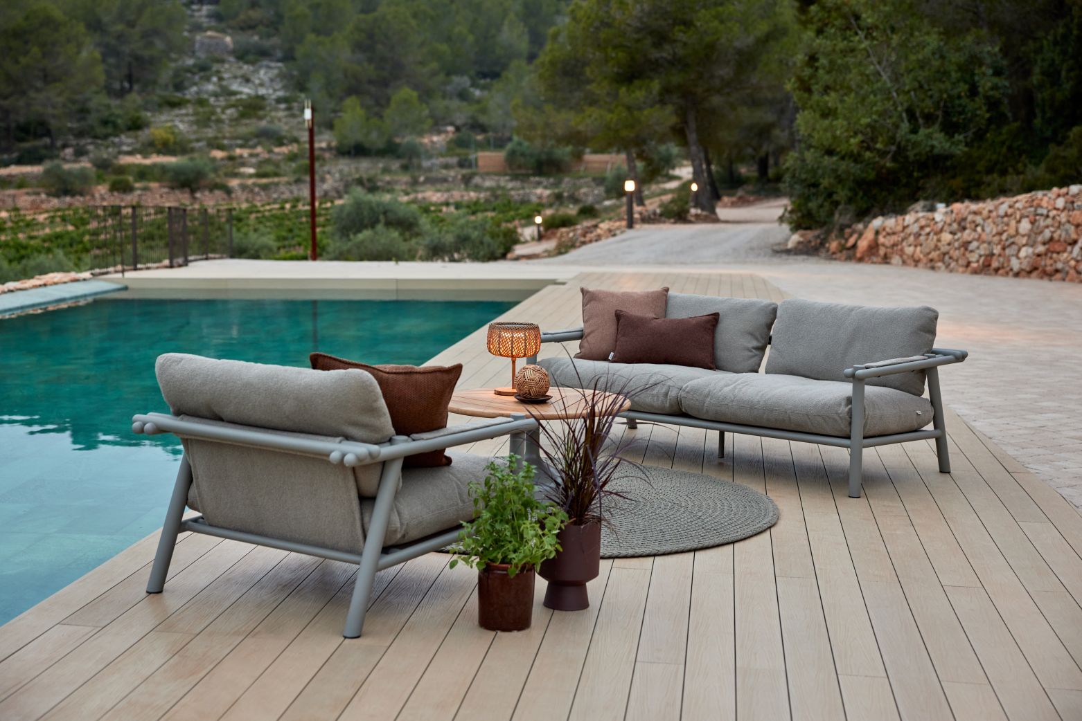 Cane-Line Illusion Glow Tischleuchte auf Outdoor-Lounge-Set am Pool. Gemütliches Ambiente mit Gartenmöbeln.