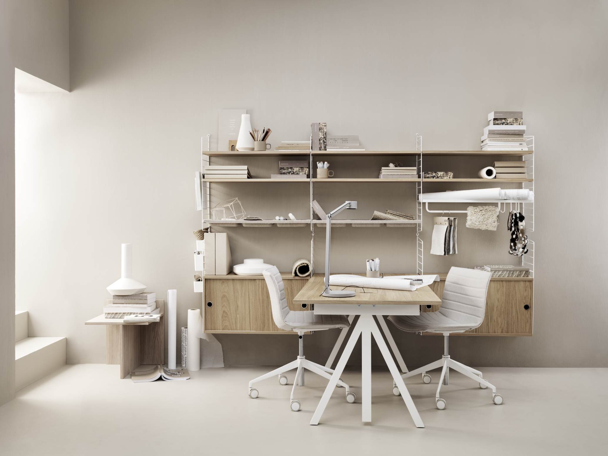 Wordesk Table Schreibtisch von String Furniture mit Regalsystem, zwei Bürostühlen und minimalistischer Dekoration in hellem Raum.