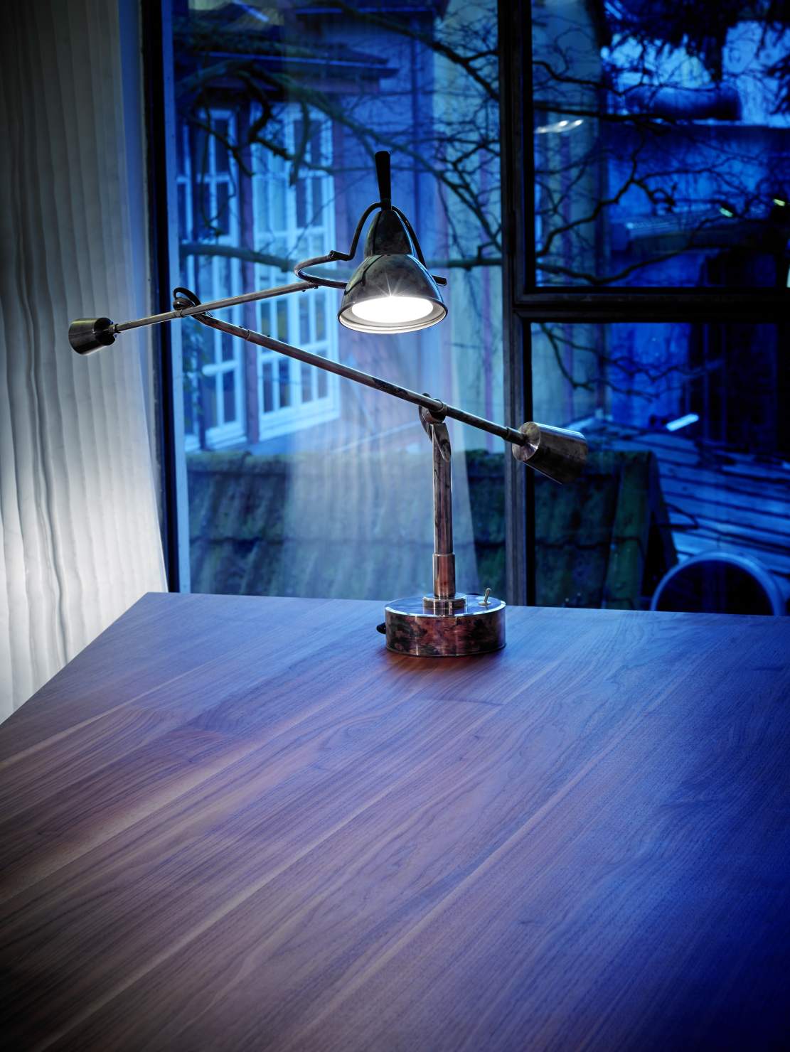 Verstellbare Schreibtischlampe aus Metall auf einem dunklen Holztisch, ideal für Büro oder Arbeitszimmer.