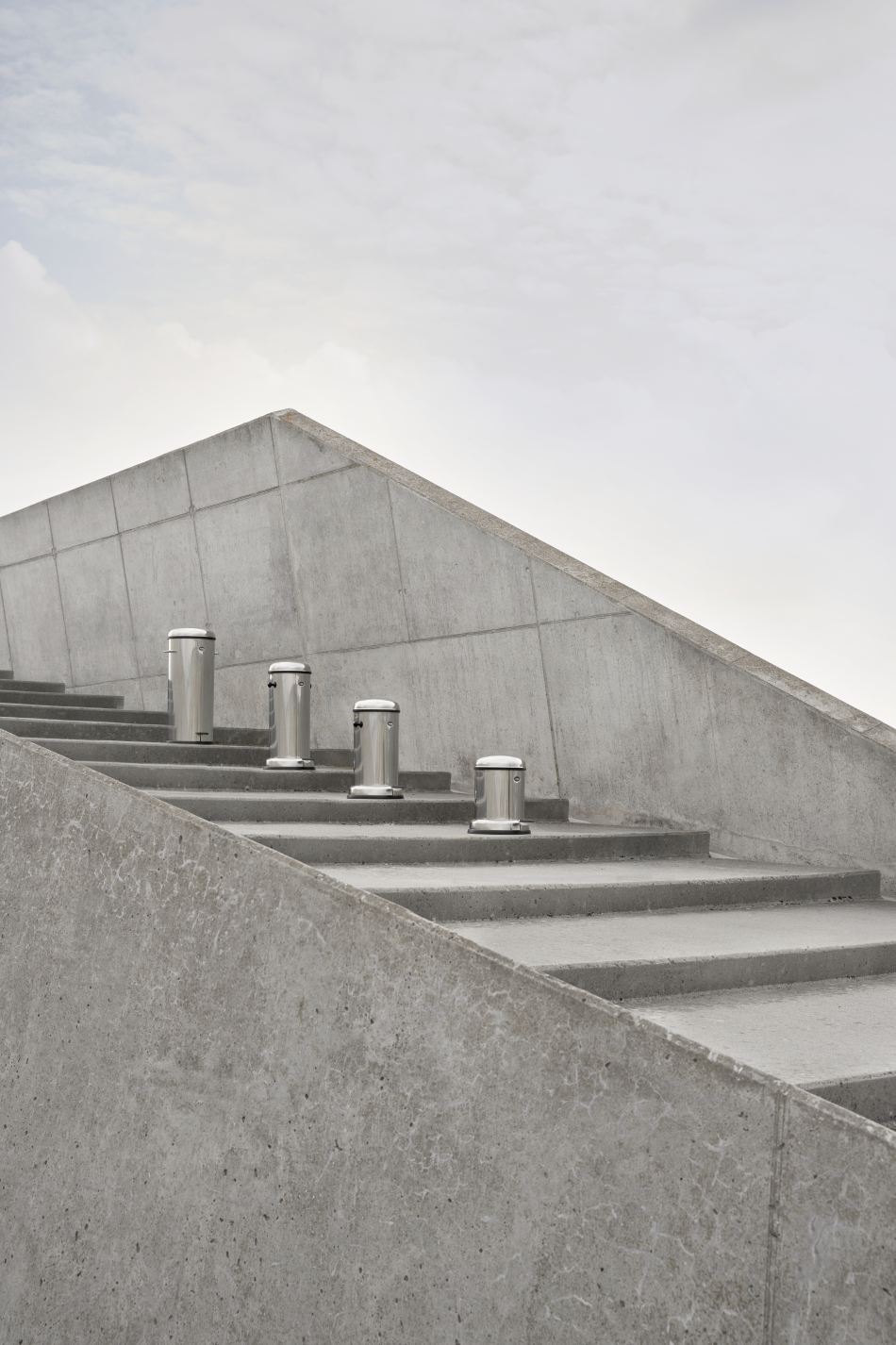 Vier Vipp Treteimer aus Edelstahl in verschiedenen Größen auf einer Betontreppe.